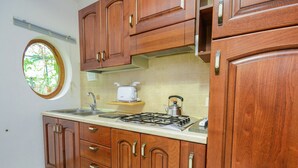 Une cuisine avec des meubles en bois, une cuisinière à gaz, un grille-pain et une fenêtre donnant sur un paysage verdoyant.