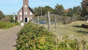 A brick church with a bell tower, a paved path, and a fenced area with vegetation. - Apartment in Bergen aan Zee near the Beach (Bergen aan zee)
