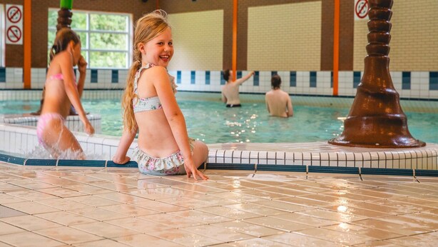 Una piscina interior con suelo y paredes de azulejos, un cartel de prohibido bañarse y un reloj en la pared.