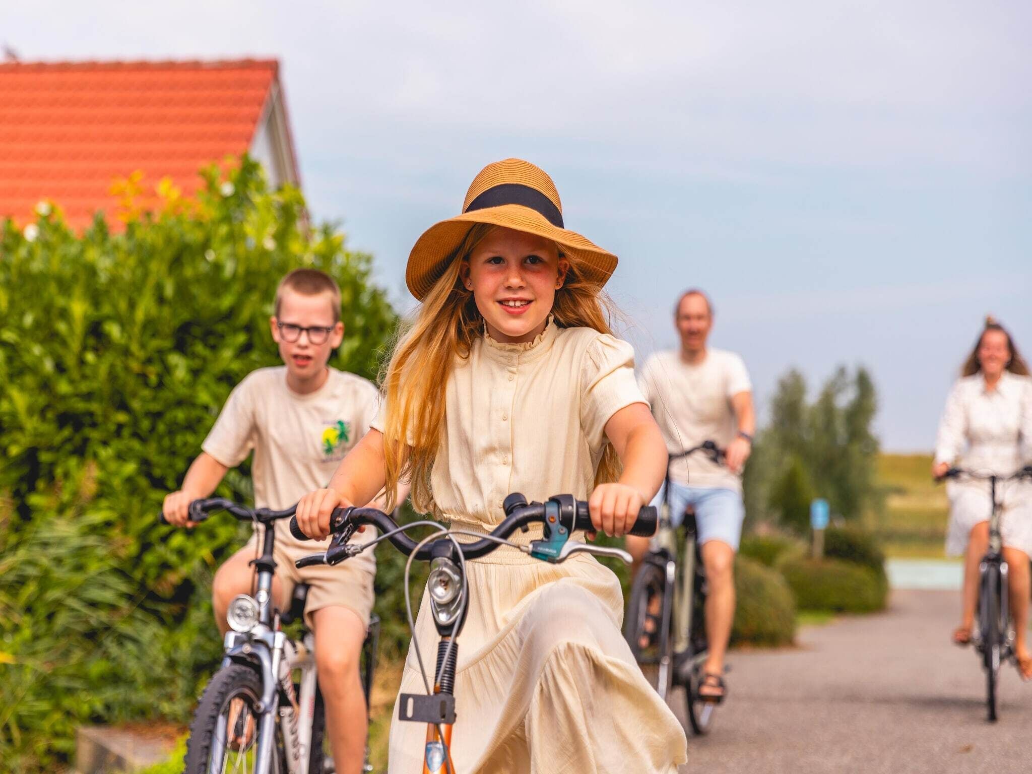 Una familia pedaleando en bicicleta por un camino pavimentado, con vegetación y un edificio al fondo.