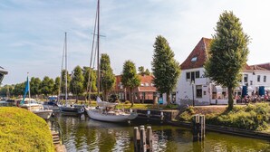 Un canal con barcos, un edificio blanco con techo rojo y una calle bordeada de árboles.