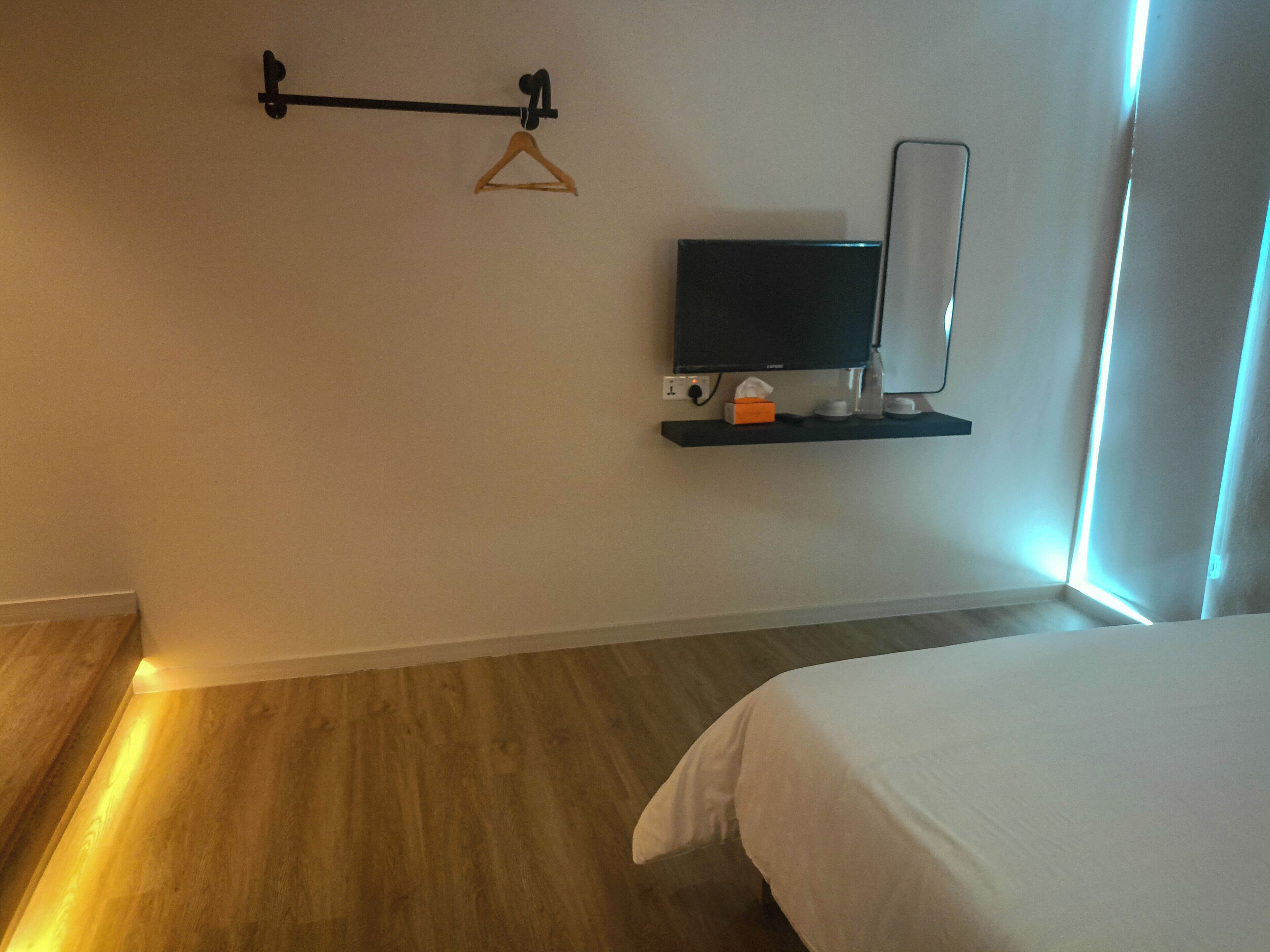 A hotel room with a bed, a TV mounted on a wall, a wooden floor, and a window with curtains.