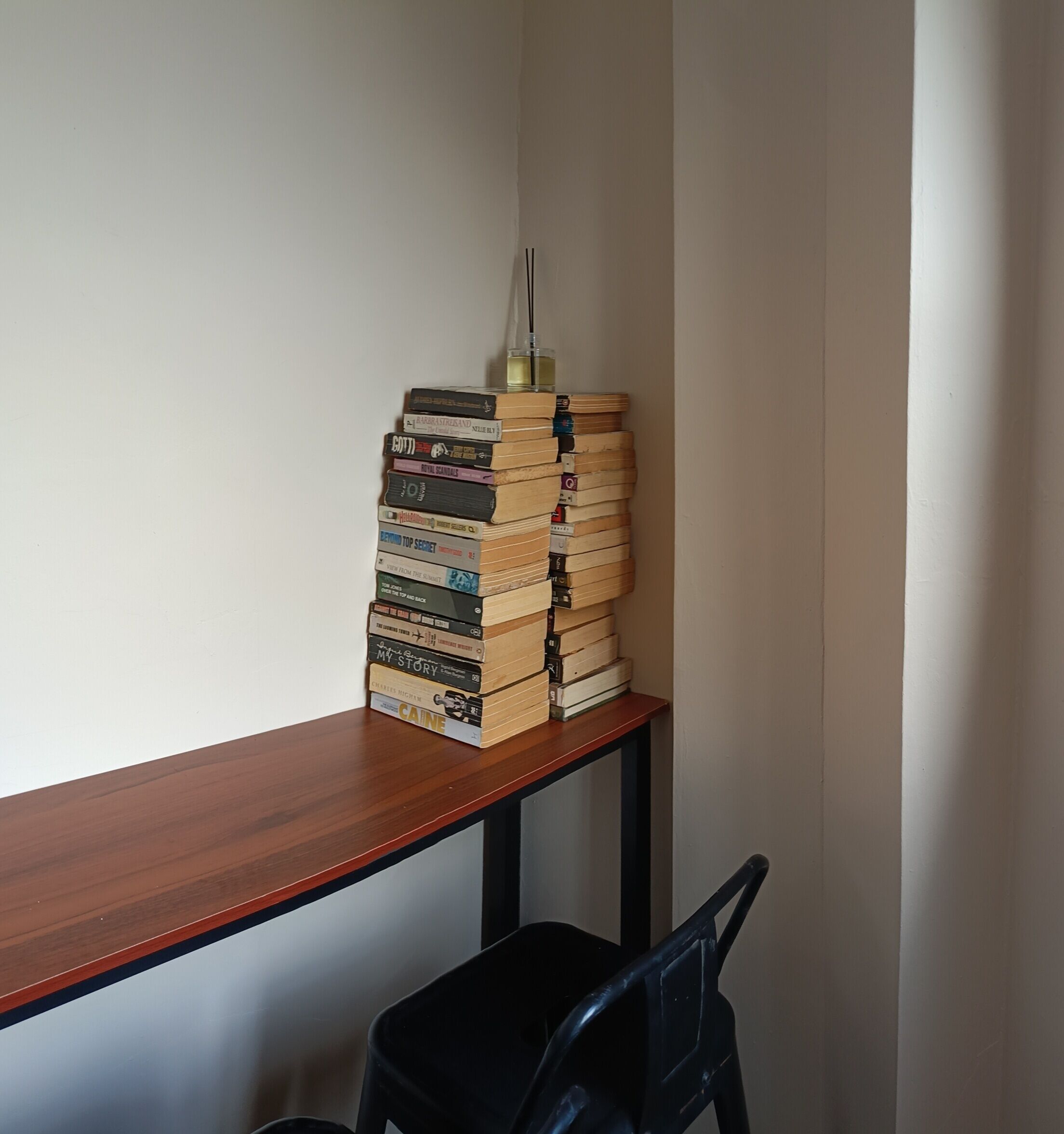 Una pila de libros sobre una mesa de madera, con una silla negra al frente.