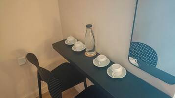 Un pequeño comedor con una mesa preparada para dos personas, una silla, un florero y un espejo que refleja una silla a lunares.