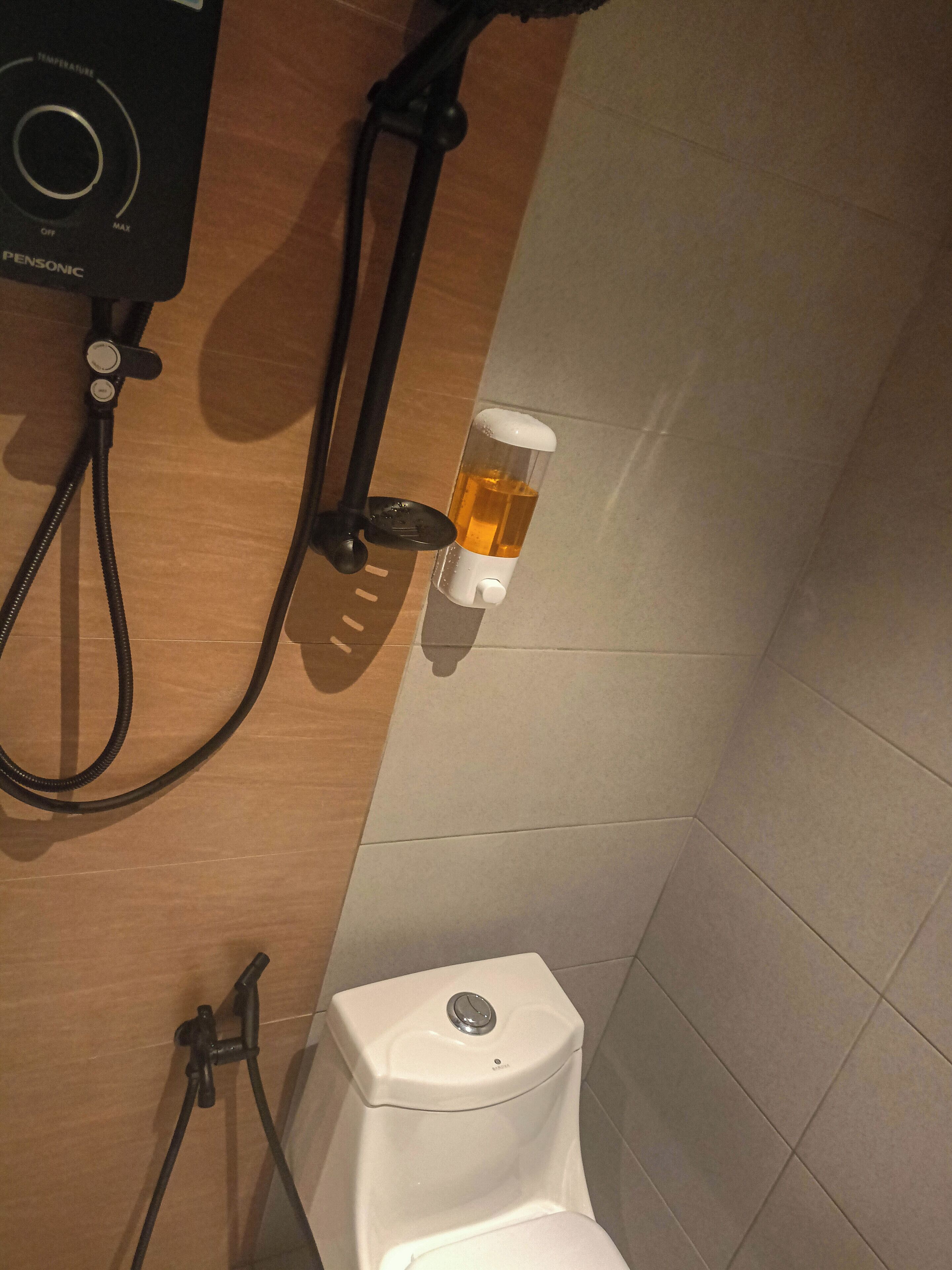 Une salle de bain équipée de toilettes, d’une douche et d’un distributeur de savon.