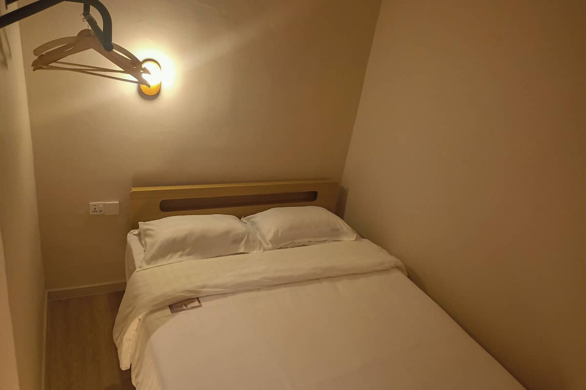 Ein kleines Zimmer mit einem Einzelbett, einem Holz-Kopfteil, weißer Bettwäsche und einer Wandleuchte.