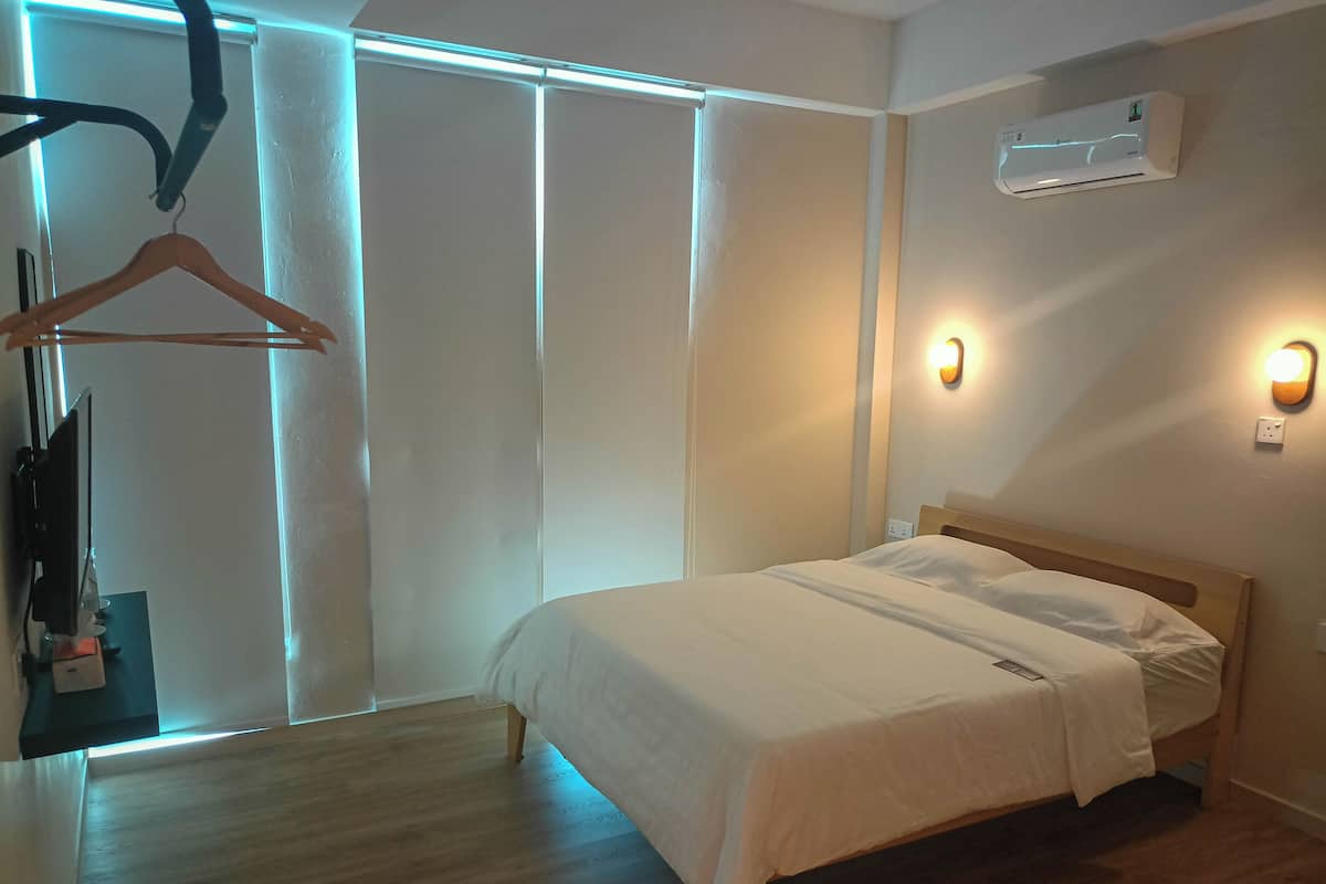 Ein Hotelzimmer mit einem Bett, Holzboden, Wandklimaanlage und einer Deckenleuchte.