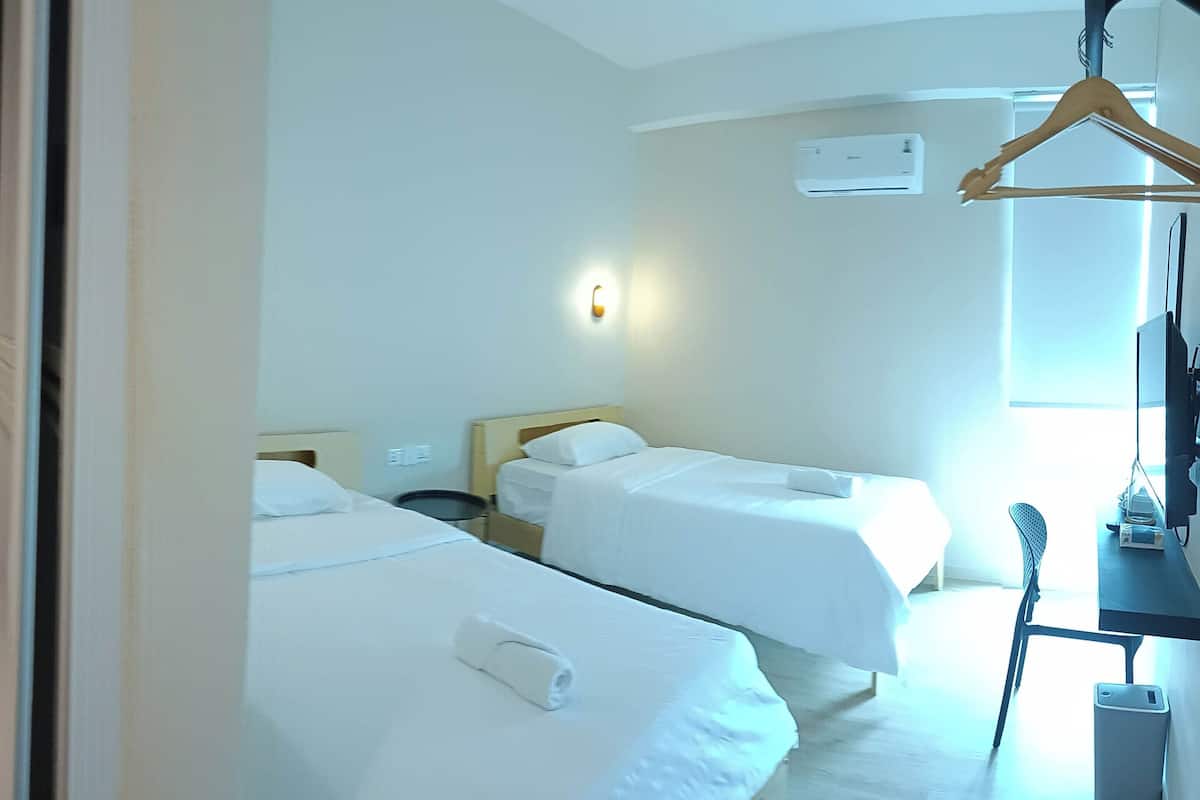 Ein Hotelzimmer mit zwei Betten, einem Nachttisch, einem Sessel, einem Kleiderhaken und einer Toilette.