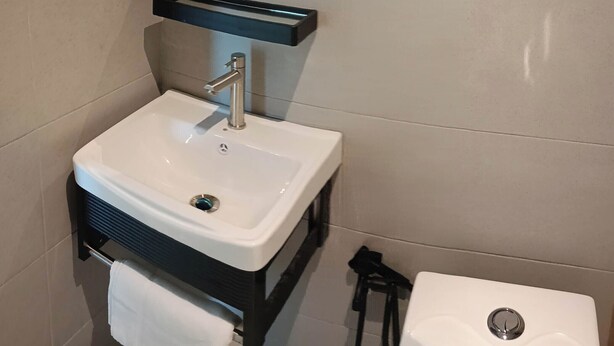 A bathroom with a white sink, a mirror above it, and a black shelf. - Keteri Boutique Hotel (Kangar)