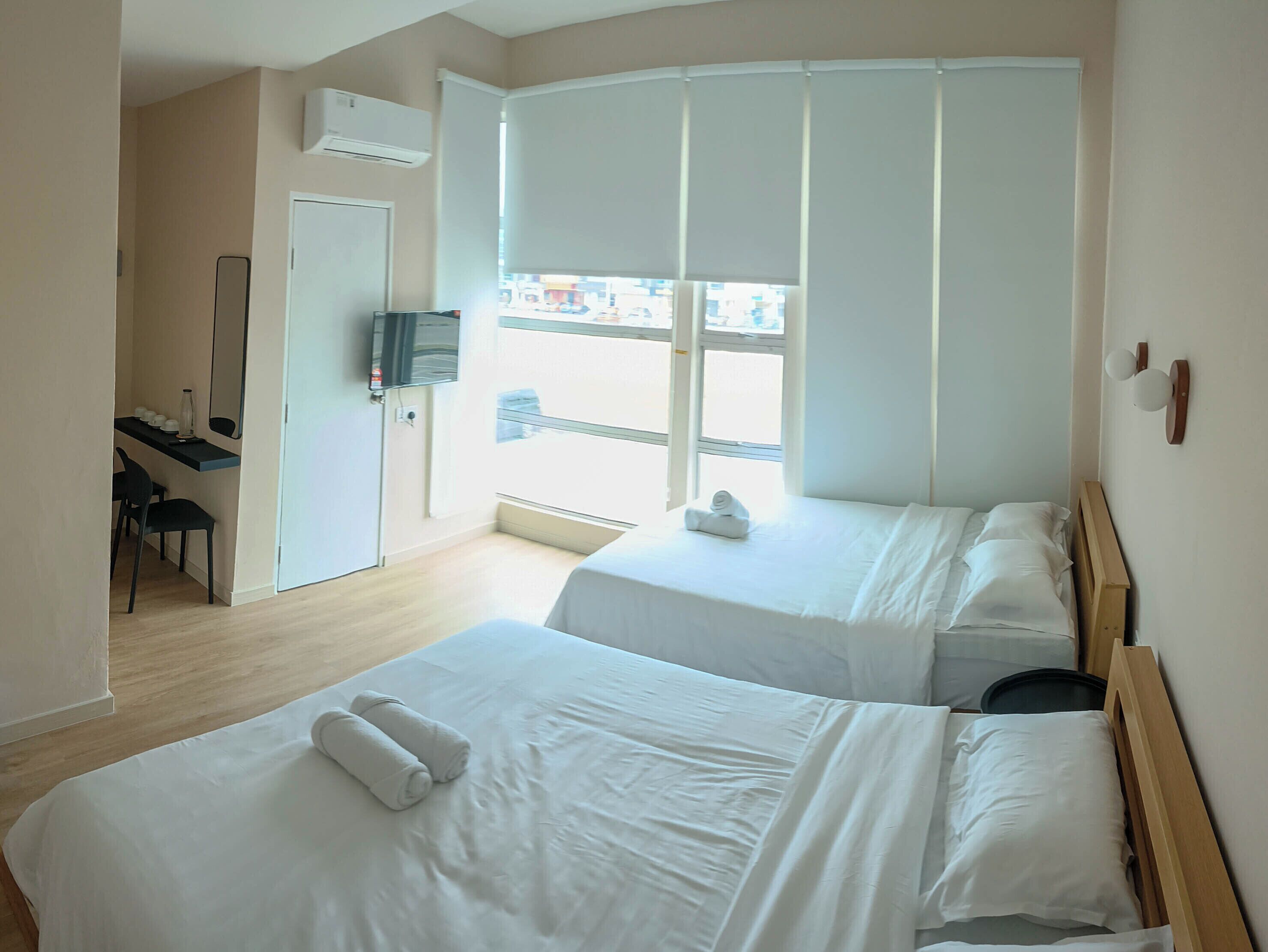 A hotel room with two beds, a desk, a chair, a TV, and a window with blinds.