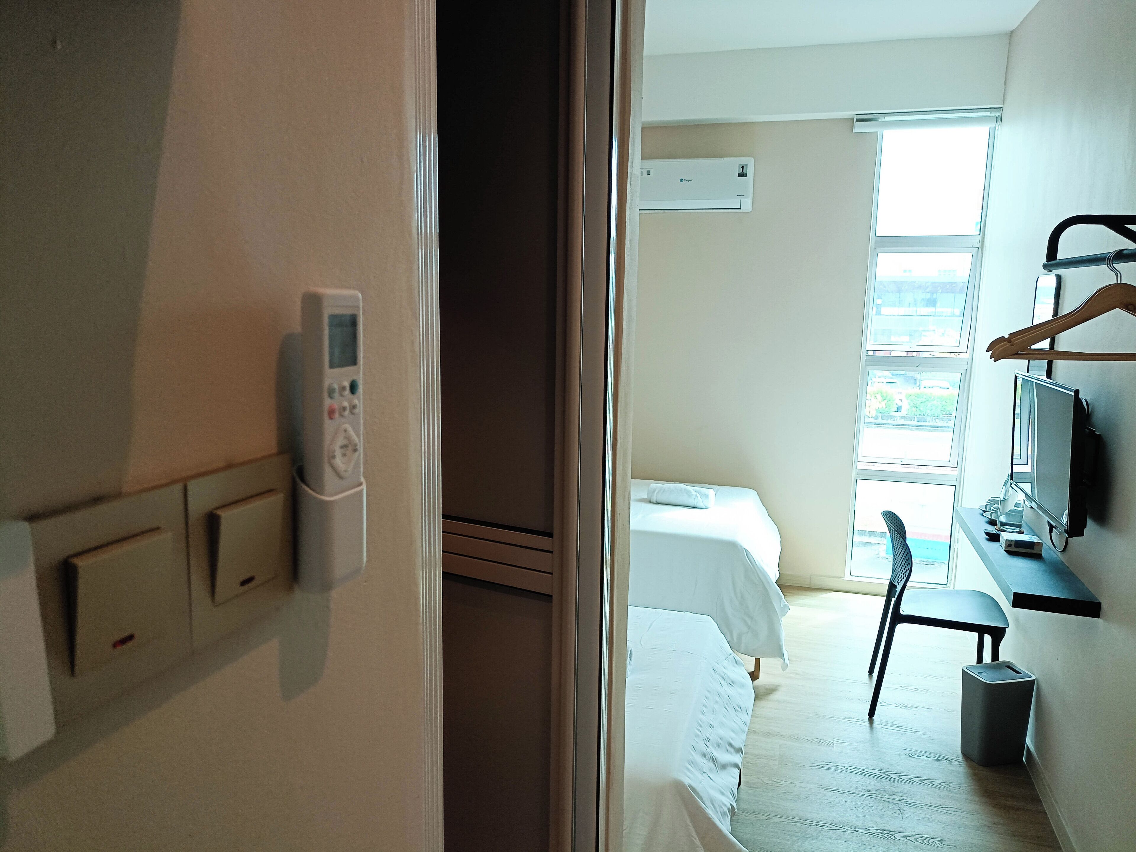 A hotel room with a bed, a chair, a desk, a TV, and an air conditioning unit.