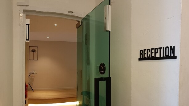 A reception area with a glass door, a reception desk, and a wall-mounted sign that reads "RECEPTION". - Keteri Boutique Hotel (Kangar)