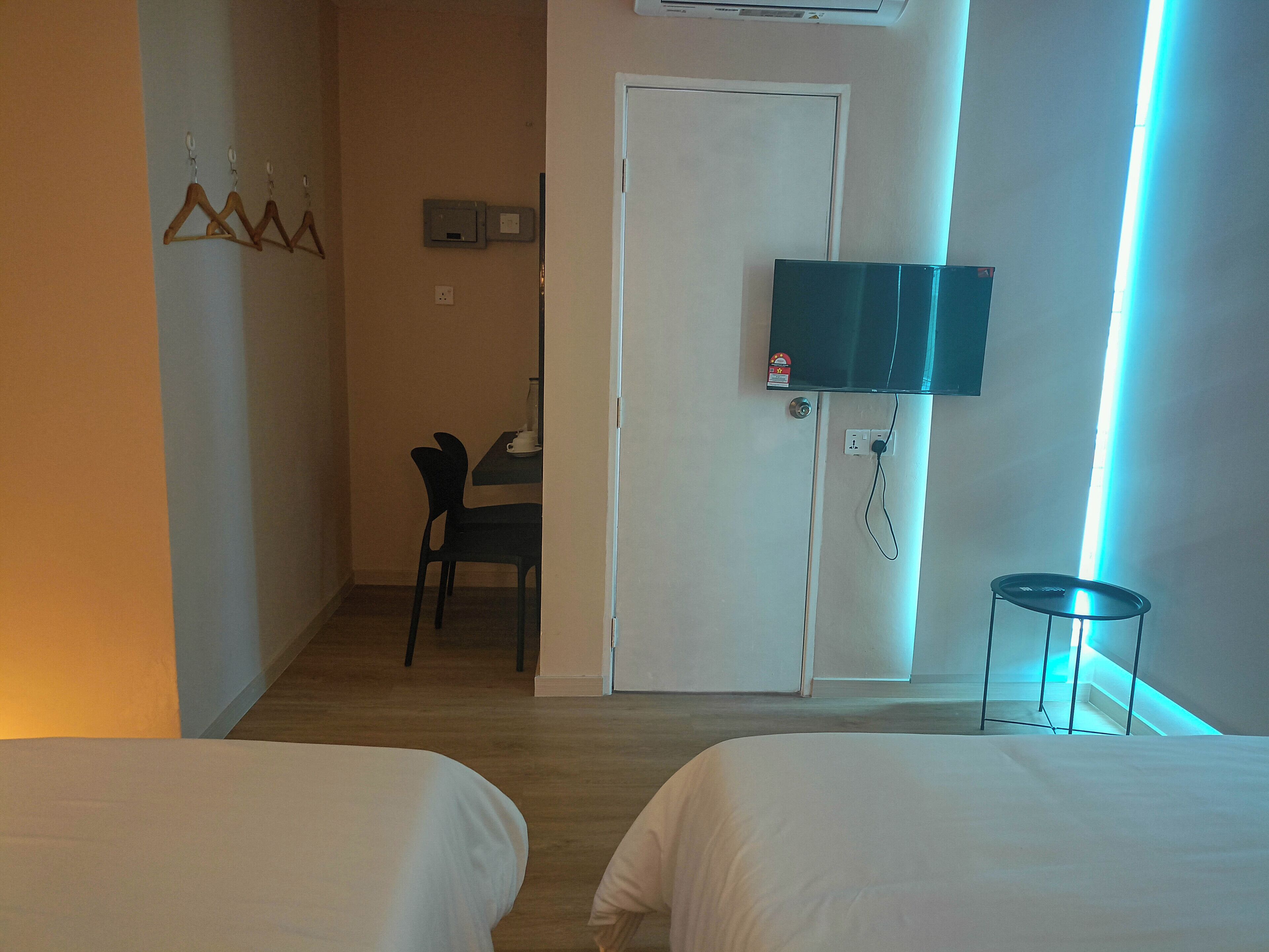 A hotel room with two beds, a desk with a chair, a TV mounted on the wall, and a door with a light switch.