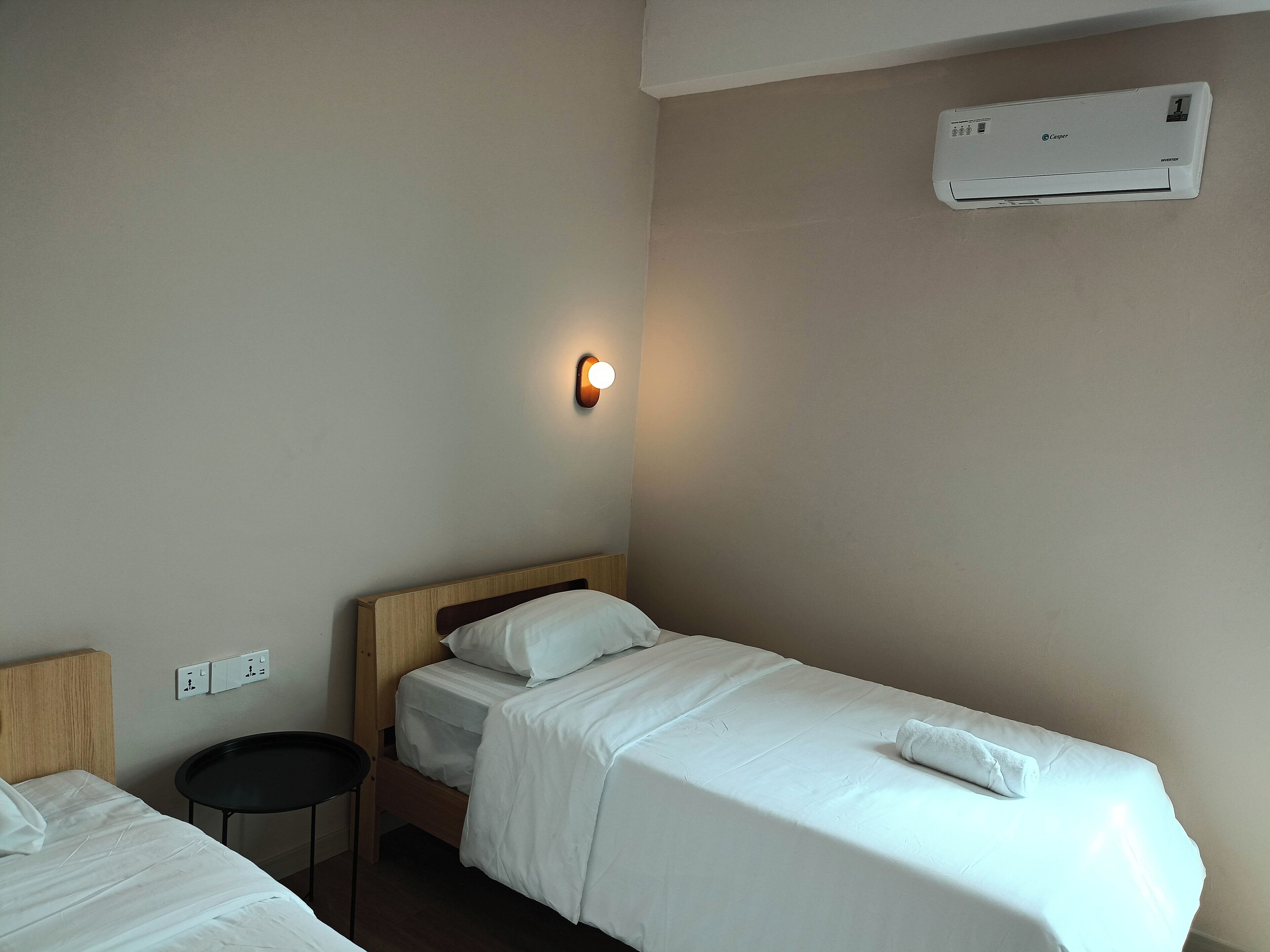 Une chambre d’hôtel avec deux lits simples, une petite table ronde, un climatiseur fixé au mur et un luminaire fixé au mur.