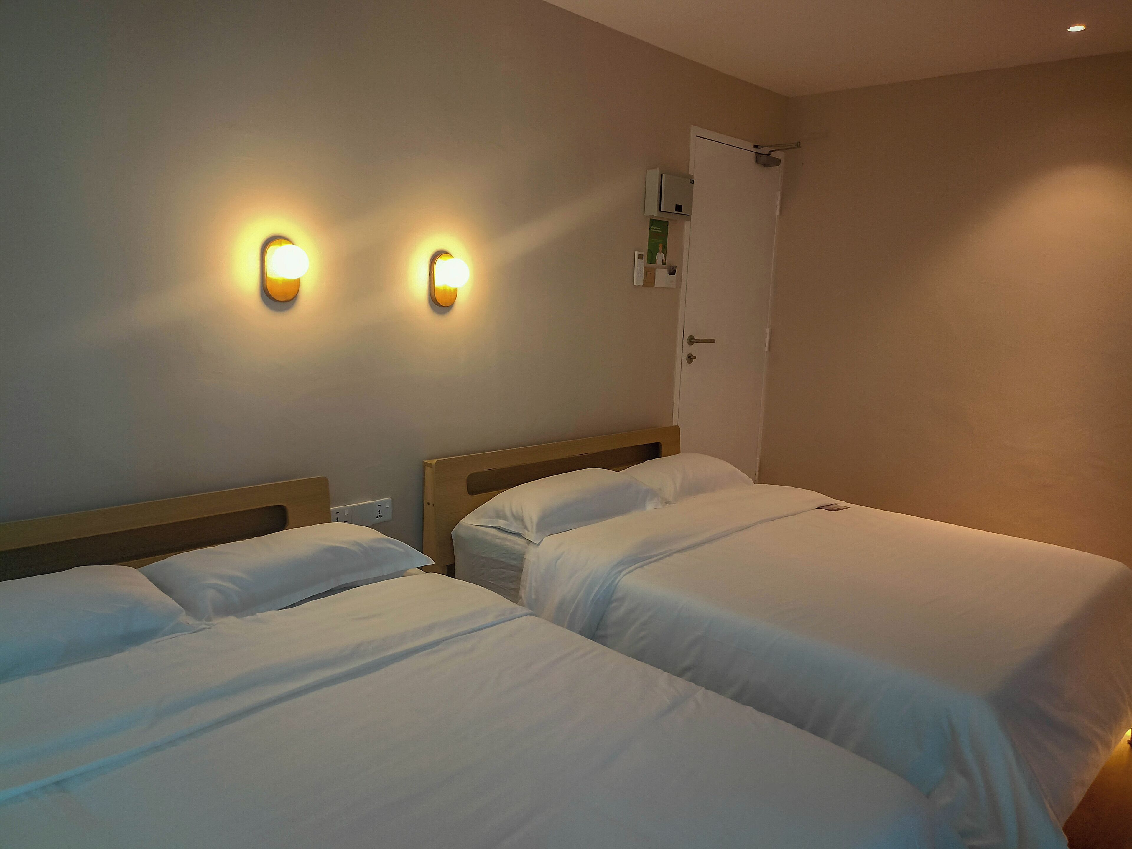 A hotel room with two beds, a door, and wall-mounted lighting.