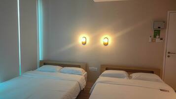 A hotel room with two single beds, a wall-mounted light fixture, a door with a lock, and a small wall-mounted device.