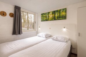 A room with two single beds, a window with curtains, a painting of a forest, and a brick wall.