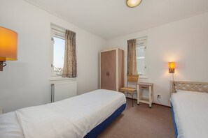 Une chambre avec deux lits, une armoire en bois, un bureau avec une chaise et deux lampes.
