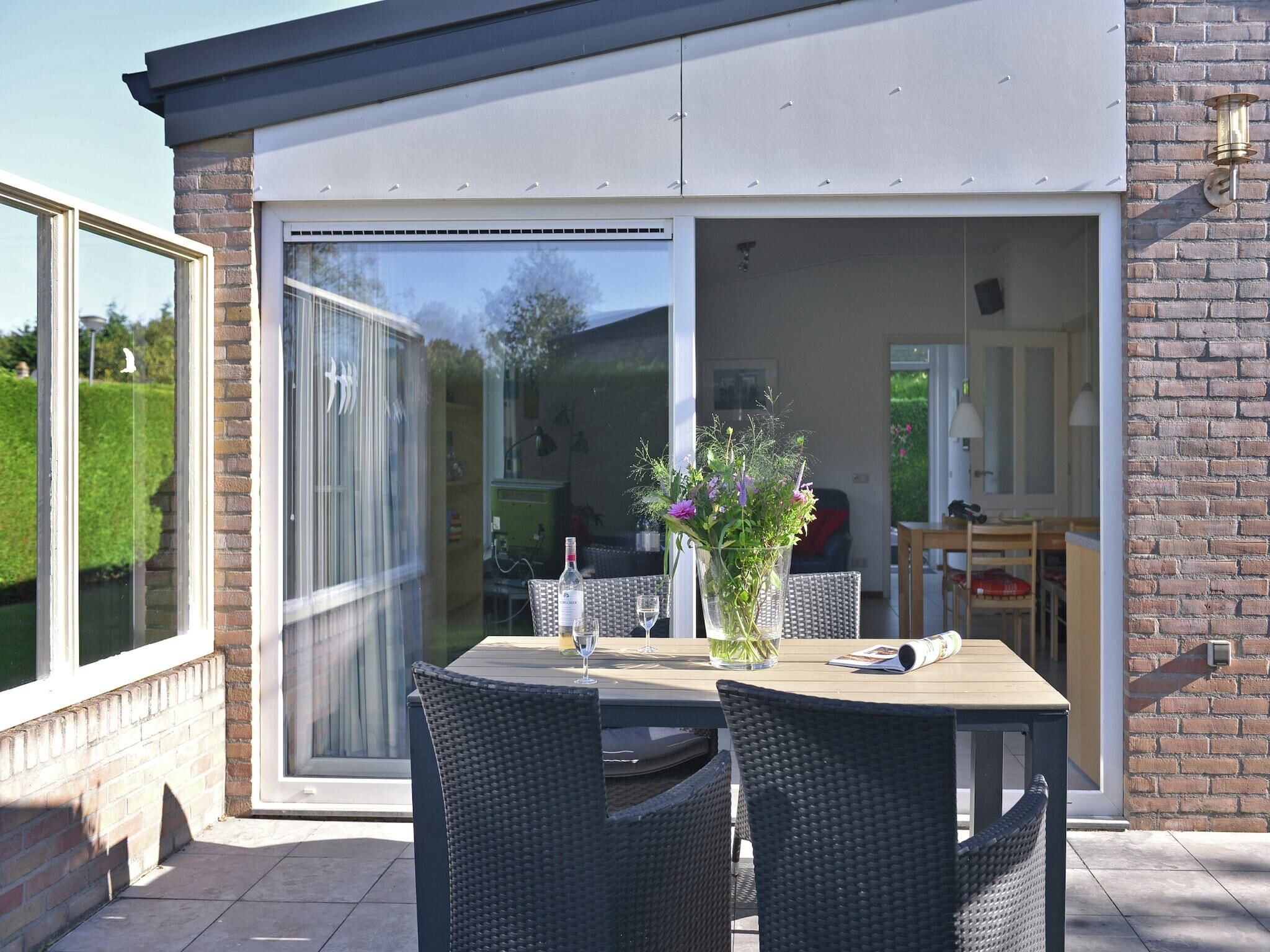 Eine Außenpatio mit Tisch und Stühlen, einer Blumenvase und einer Glasschiebetür zu einem Innenraum.