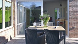 Eine Außenpatio mit Tisch und Stühlen, einer Blumenvase und einer Glasschiebetür zu einem Innenraum.