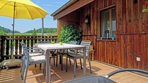 A wooden deck with a table and chairs, a yellow umbrella, and a view of the countryside.