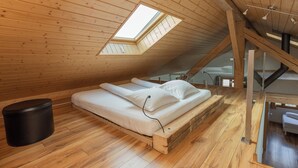 A loft bedroom with a skylight, wooden flooring, a bed, and a small black trash bin.
