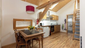 A kitchen with wooden beams, a dining table with chairs, a red pendant light, and a view of the bathroom.