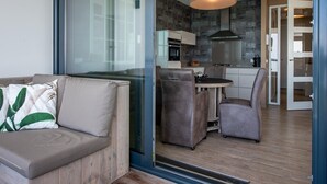 A modern living room with a glass wall, a sofa, and a dining area with chairs and a table. - Apartment in Veere with Lake Views & Marina (Kamperland)