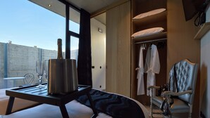 A hotel room with a bed, a bedside table with a champagne bottle and glasses, a wardrobe with hanging robes, and a chair. - Dalhem Villa with Garden (Dalhem)
