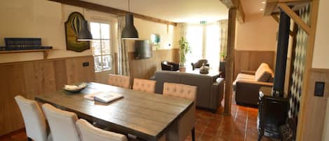 A dining area with a wooden table and chairs, a kitchen in the background, and a fireplace.