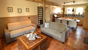 Un salon chaleureux avec deux canapés, une table basse et un coin repas, avec une cuisine en arrière-plan.