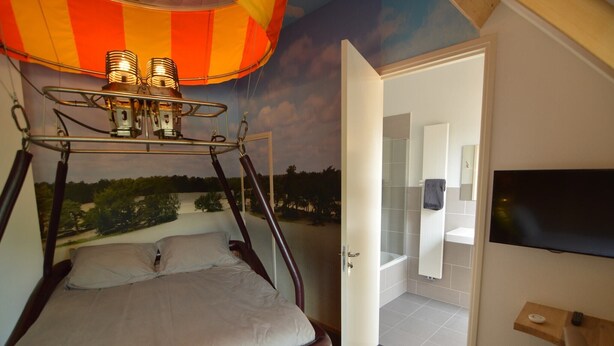 Une chambre avec une fresque représentant une montgolfière, un lit et un téléviseur fixé au mur.