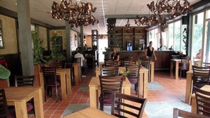 Een restaurantinterieur met houten tafels en stoelen, een bar en grote ramen voor natuurlijk licht.