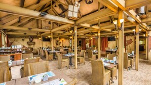 Un'ampia sala ristorante con soffitti alti, travi a vista e arredamento rustico. I tavoli sono apparecchiati con sedie in vimini e portatili, a indicare un ambiente moderno ideale per lavorare.