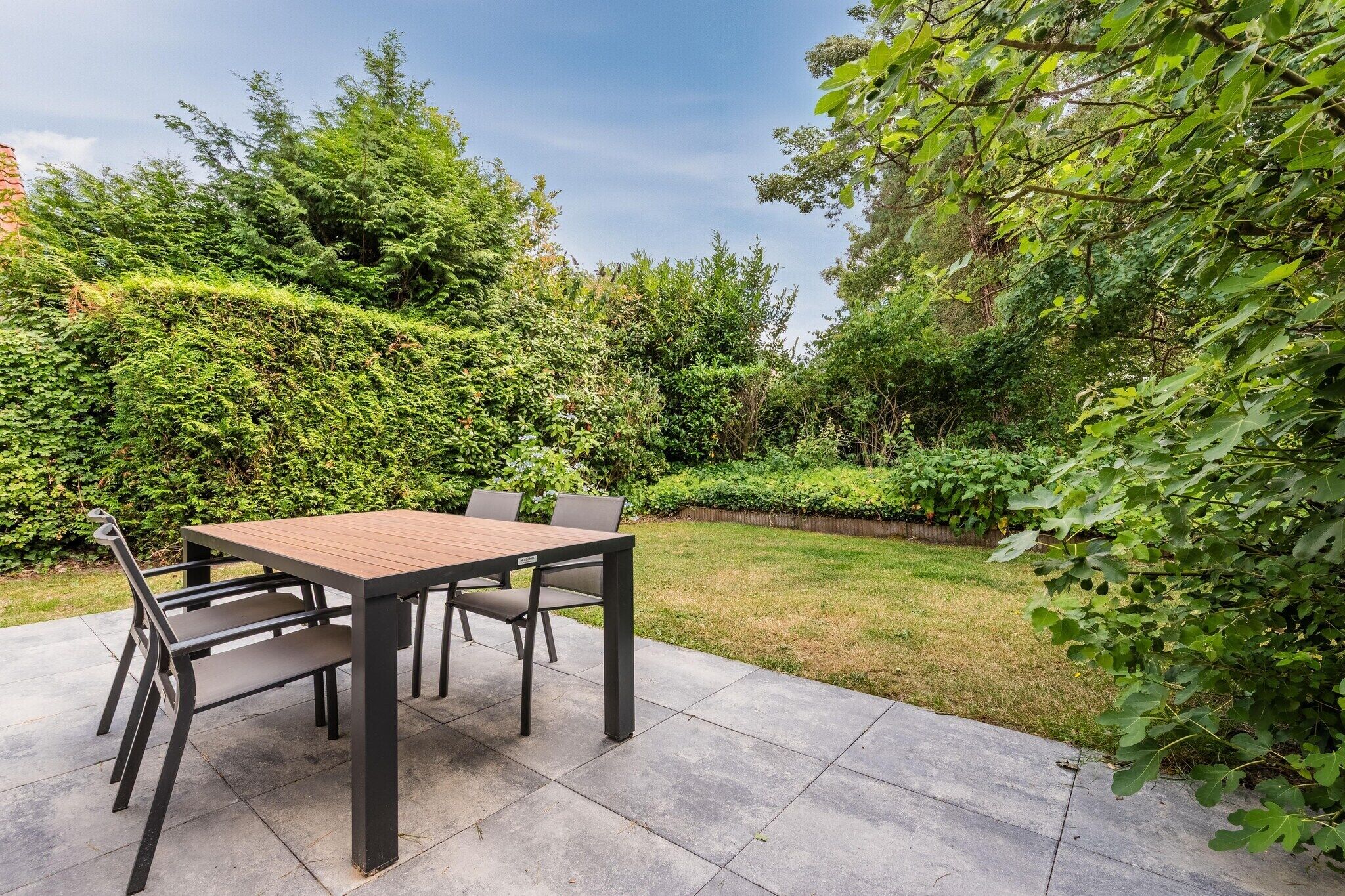 An outdoor patio with a table and chairs, surrounded by lush greenery.