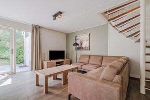 A modern living room with a sofa, a coffee table, a TV, and a staircase. - Charming Villa in Natural Surroundings (Arcen)