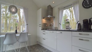 Una cocina moderna con armarios blancos, una zona de comedor con dos sillas y un ventanal con cortinas.