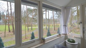 Una habitación con amplios ventanales, un radiador y vistas a un parque con árboles y césped.