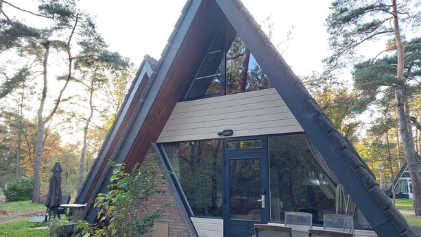 A modern, triangular-shaped building with a large glass door and windows, surrounded by trees and a patio area with outdoor furniture. - Chalet in Tyrol near Ski Slope (Stramproy)