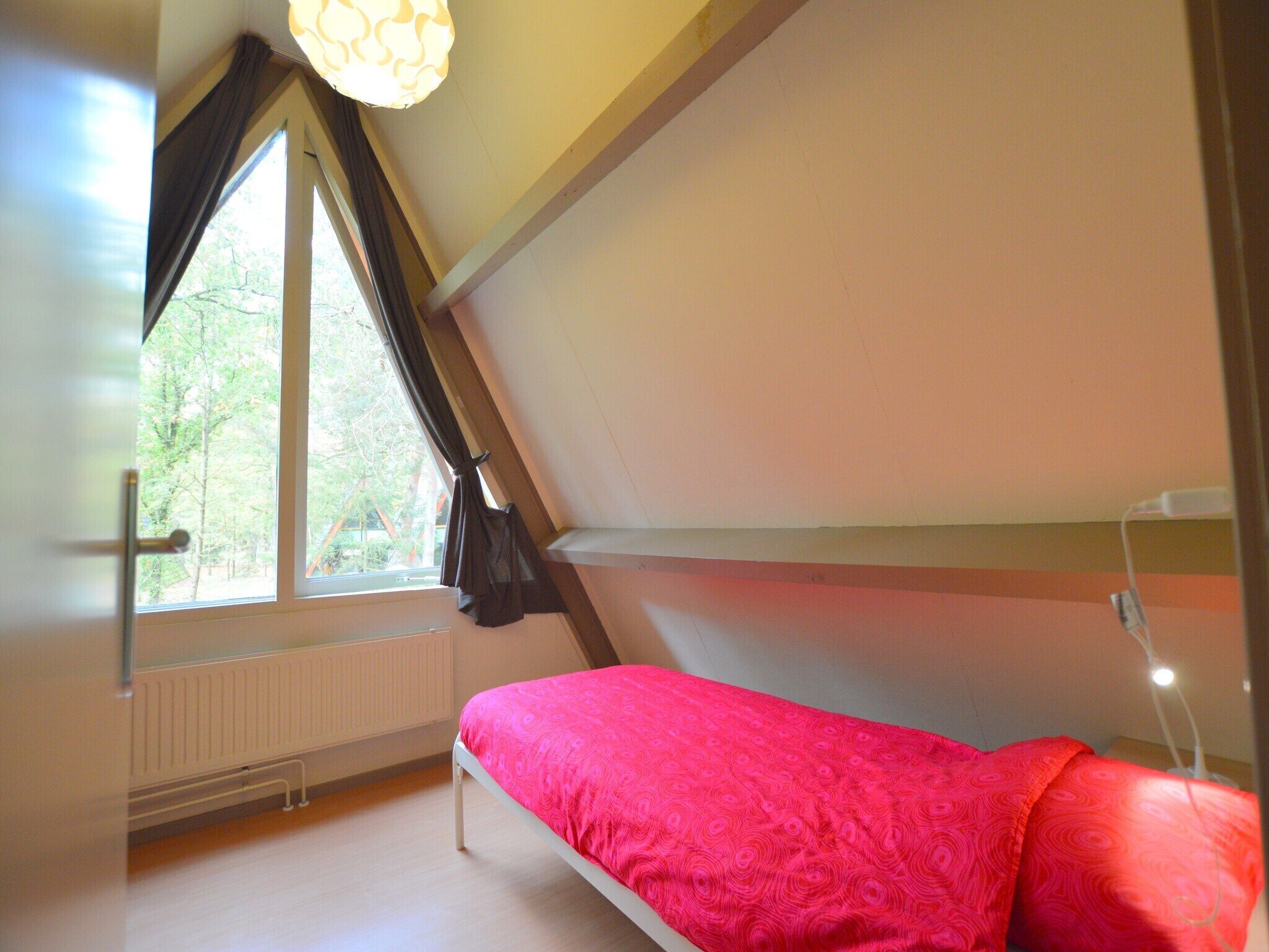 Une chambre de type dortoir, avec un lit superposé, une fenêtre avec des rideaux, un radiateur et un luminaire au plafond.