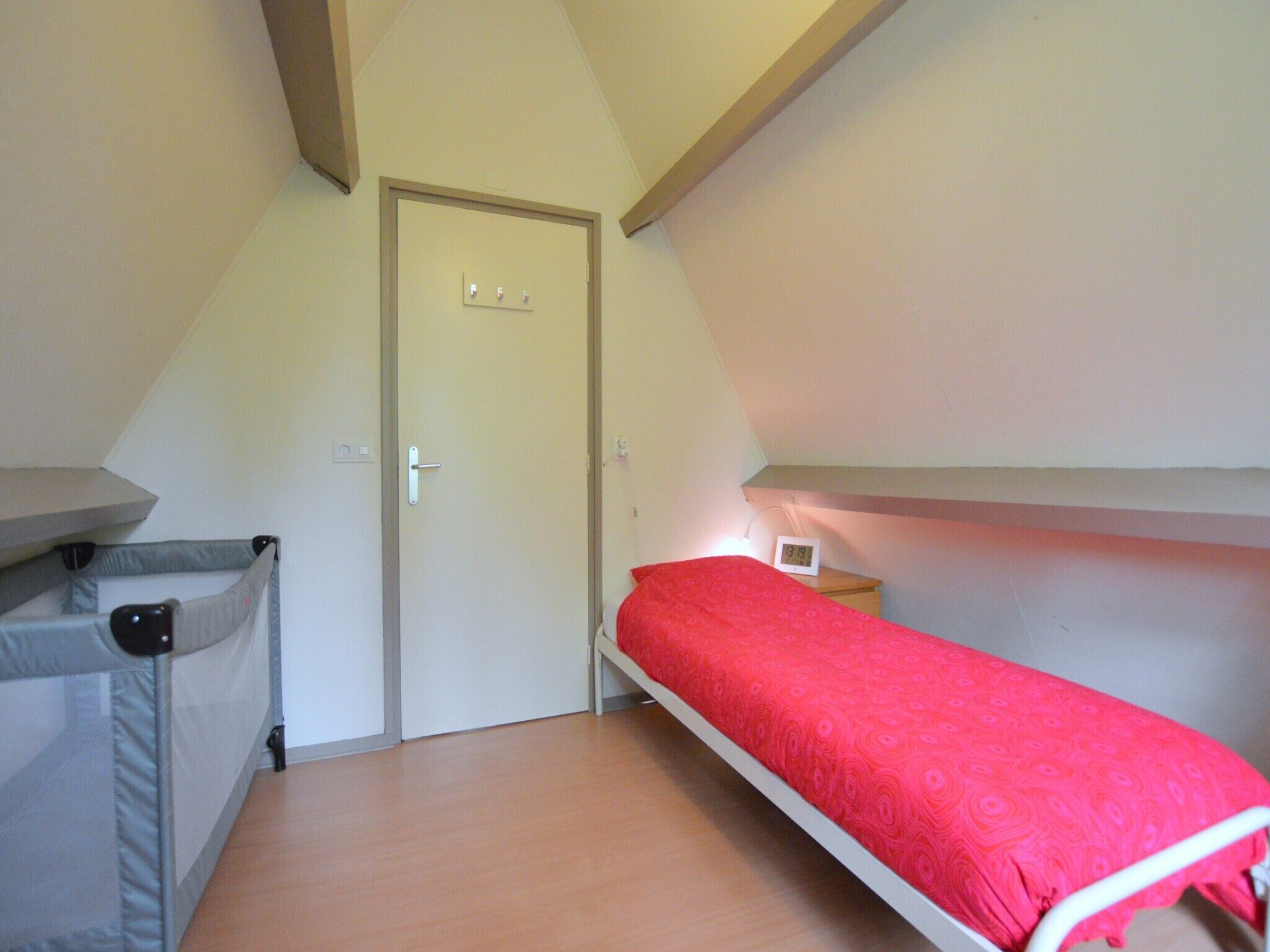 Een kleine, driehoekige kamer met een stapelbed, een deur en een nachtkastje met een lamp.