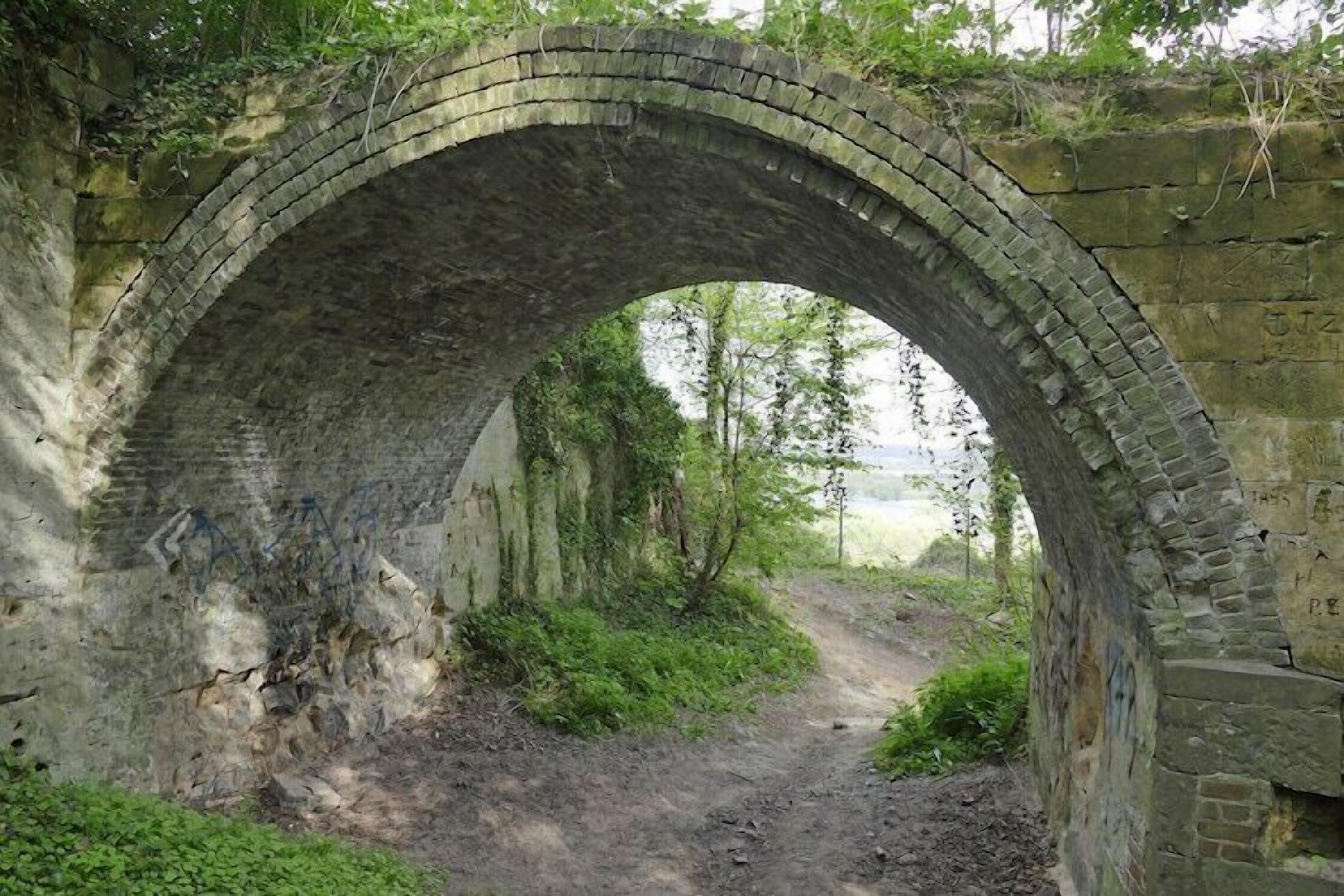 An old stone bridge with a dirt path leading through it.