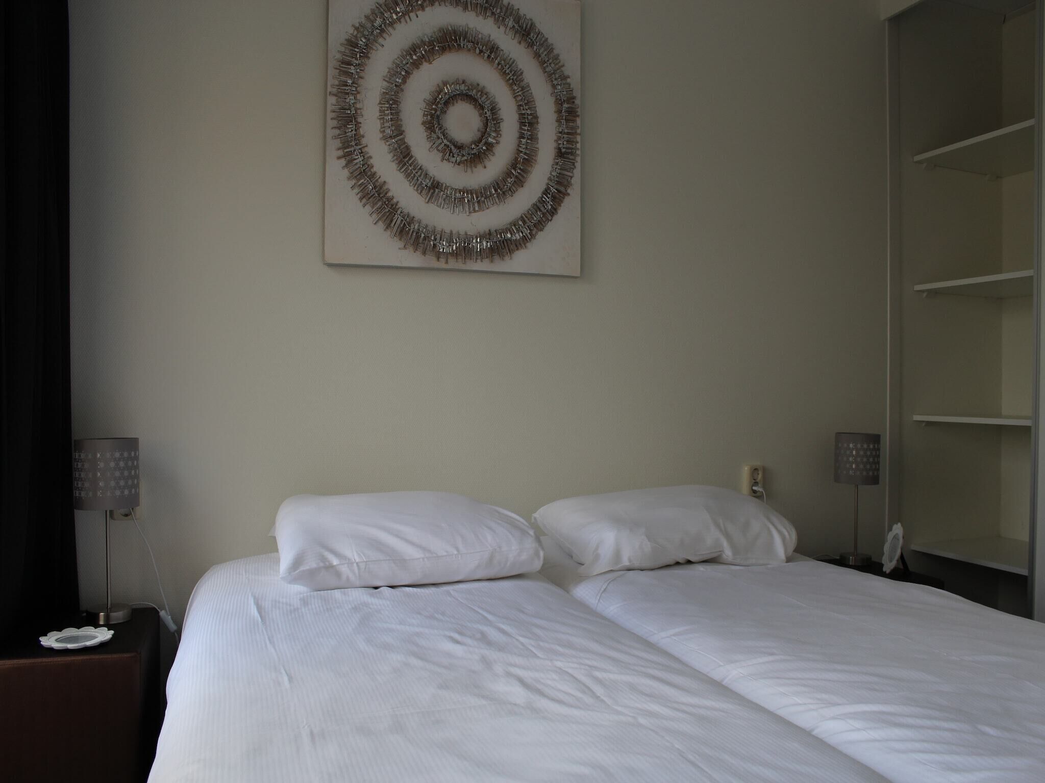 Habitación de hotel con cama doble, dos mesitas de noche, un adorno en la pared y un armario.
