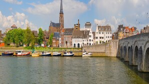 A river with boats docked, a bridge, and historic buildings including a church with a tall spire. - Charming Retreat for Your Escape (Bemelen)