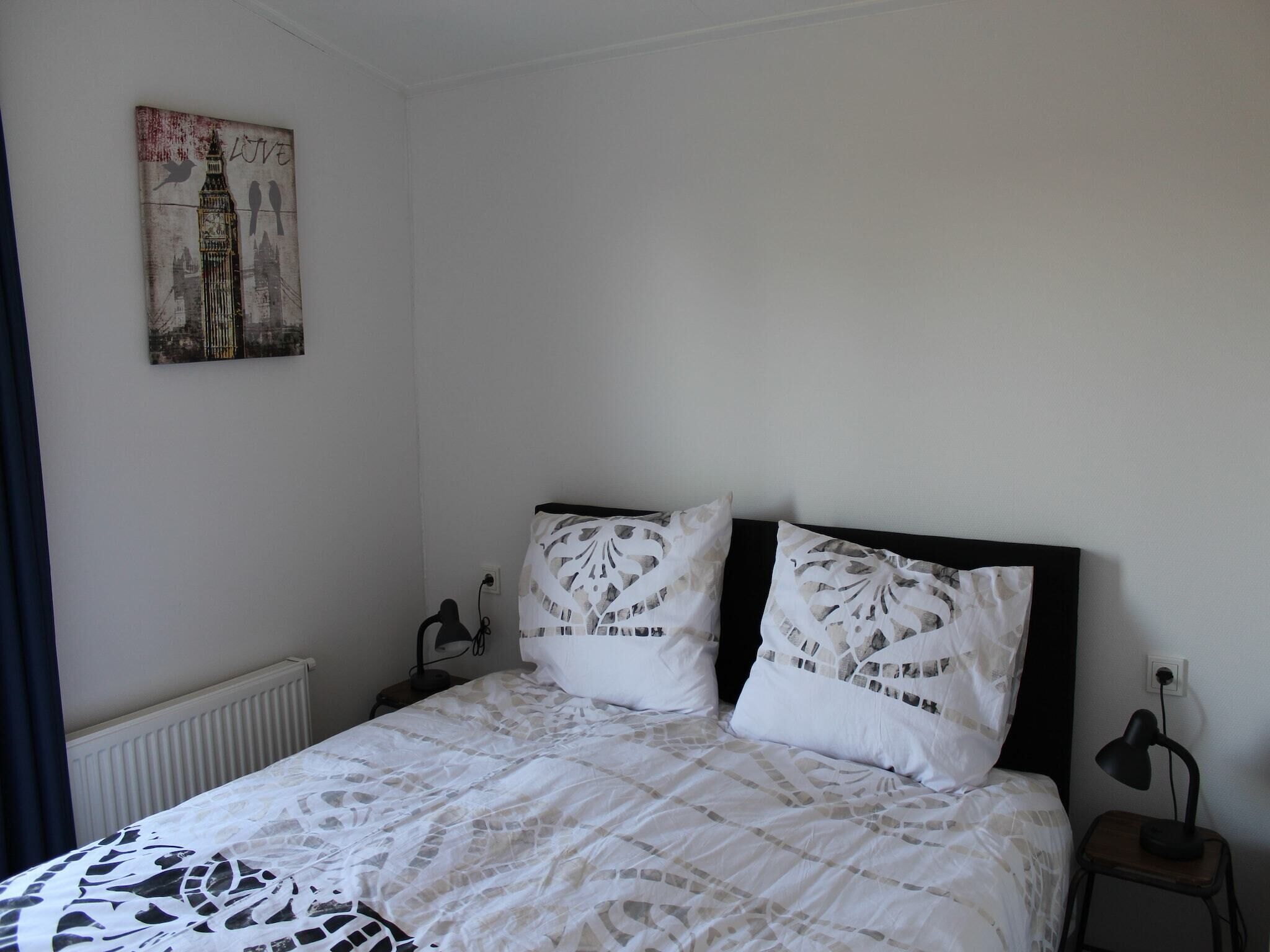 A bedroom with a bed, two pillows, a nightstand, a lamp, and a wall-mounted picture.
