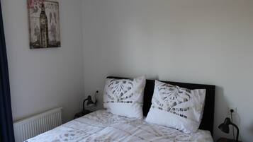 A bedroom with a bed, two pillows, a nightstand, a lamp, and a wall-mounted picture.