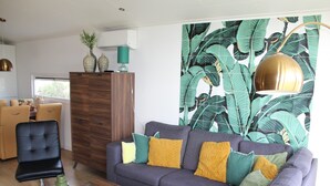 Un salón moderno con un sofá gris, una mesa de centro de madera y un llamativo papel tapiz tropical.