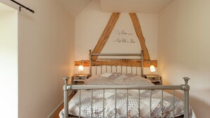 A bedroom with a metal bed frame, two bedside lamps, a wooden ceiling beam, and a wall with a decorative inscription. - Scenic Gulp Valley Stay (Slenaken)