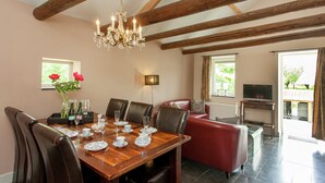 A dining area with a wooden table set for six, surrounded by leather chairs. A chandelier hangs from the ceiling, and there is a red sofa in the background. - Scenic Gulp Valley Stay (Slenaken)