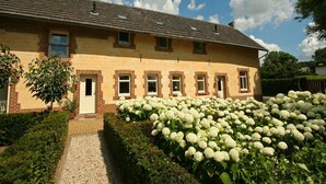 A two-story house with a brick facade, multiple windows, and a garden with white hydrangea flowers. - Wijlre Farmhouse stay (Wijlre)